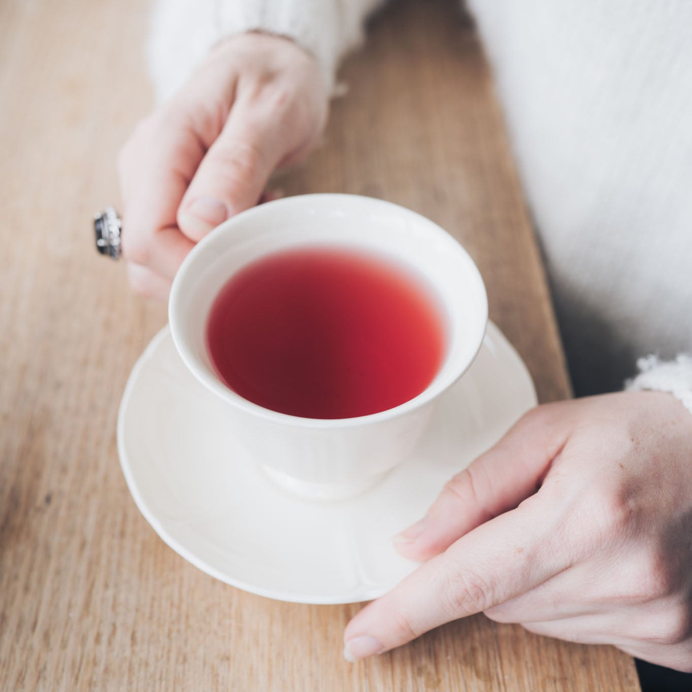 Person holding a white teacup with red tea on a wooden table