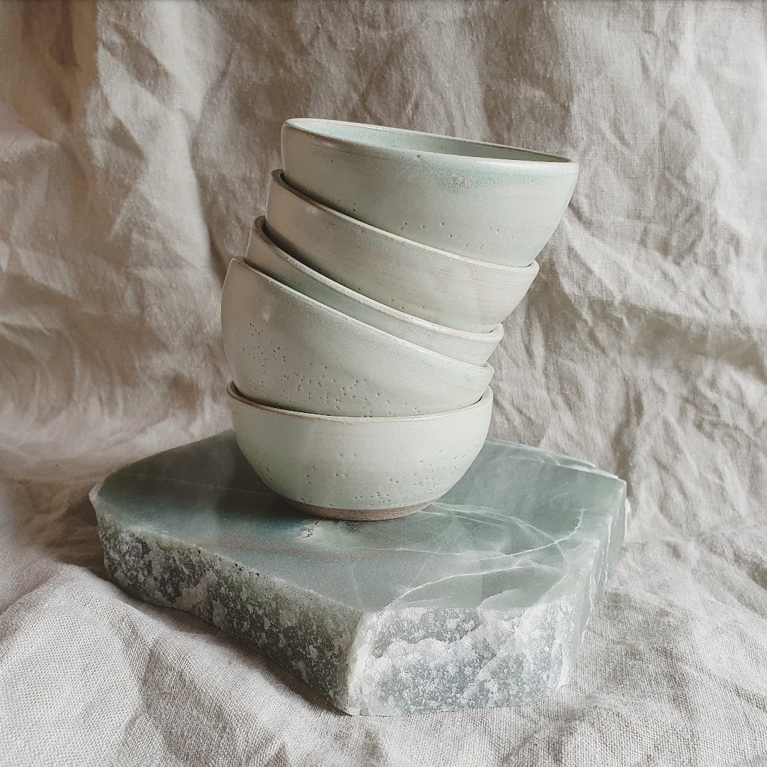 5 wonkily stacked bowls on top of flat smooth raw stone.